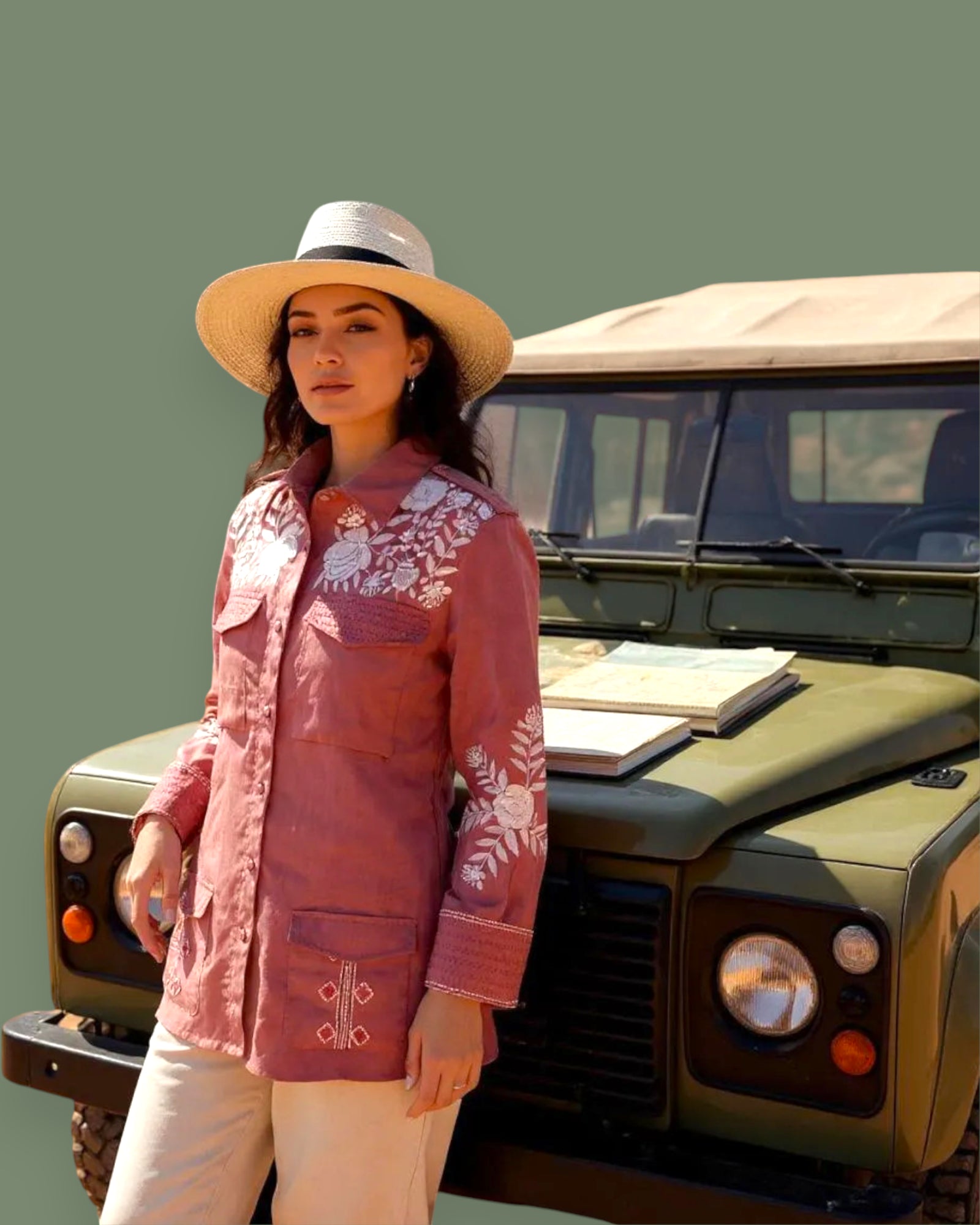 Woman in a pink embroidered jacket and standing next to a green jeep.