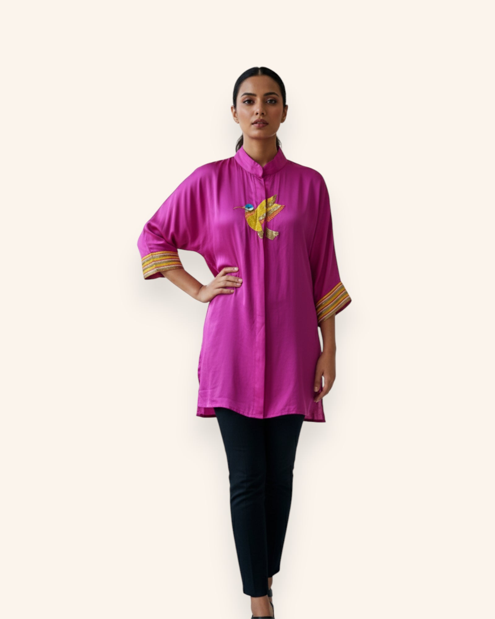 Woman wearing a bright pink top with a yellow Embroidery design on a white background