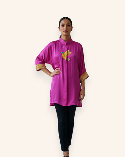 Woman wearing a bright pink top with a yellow Embroidery design on a white background