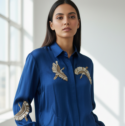 Woman wearing a blue shirt with gold embroidery in a bright room
