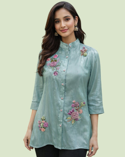 Woman wearing a light blue embroidered shirt on a light green background