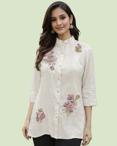 Woman wearing a white embroidered shirt with floral designs on a light green background