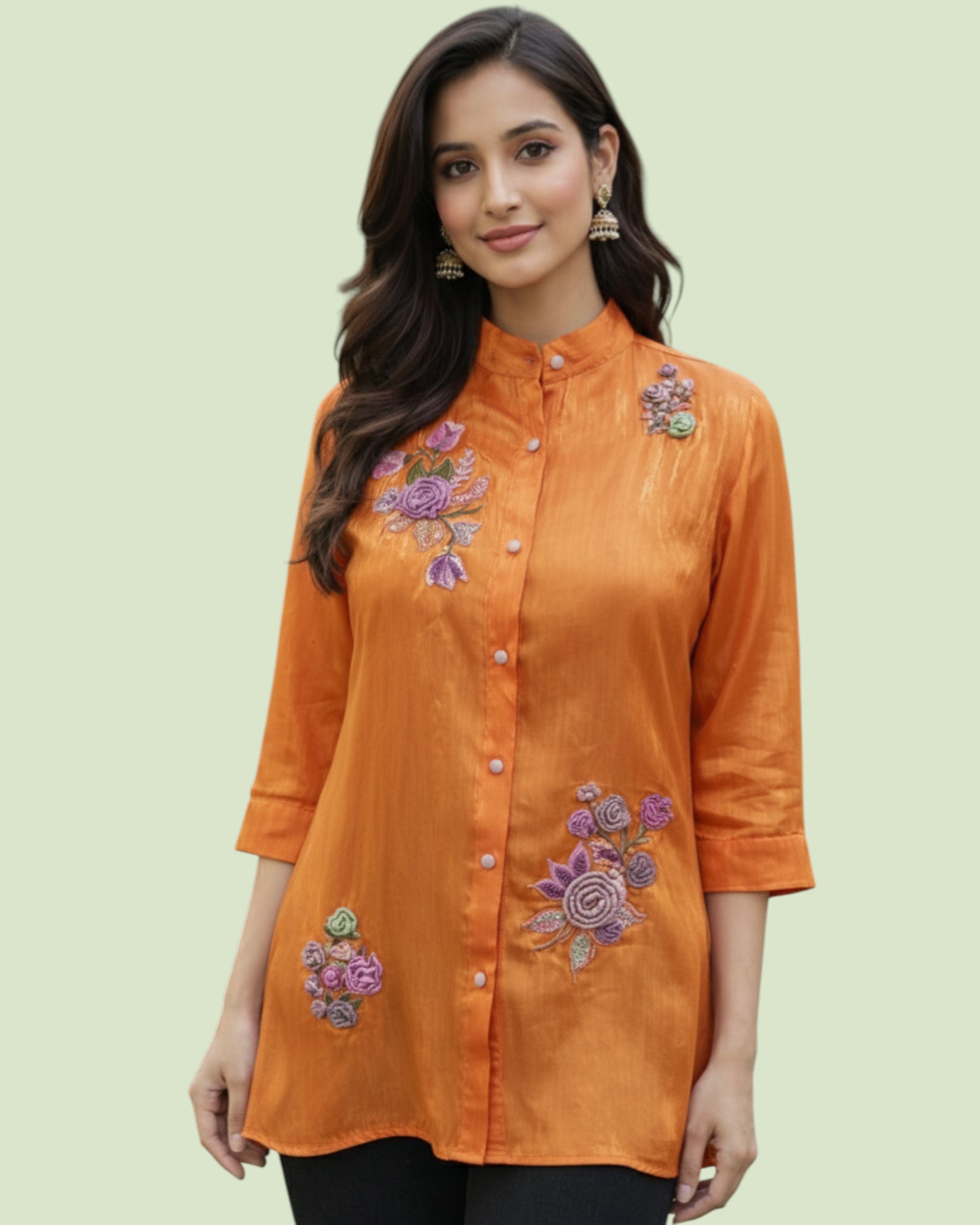 Woman wearing an orange embroidered shirt on a light green background