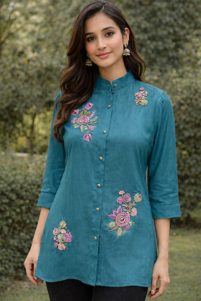 Woman wearing a teal embroidered shirt.