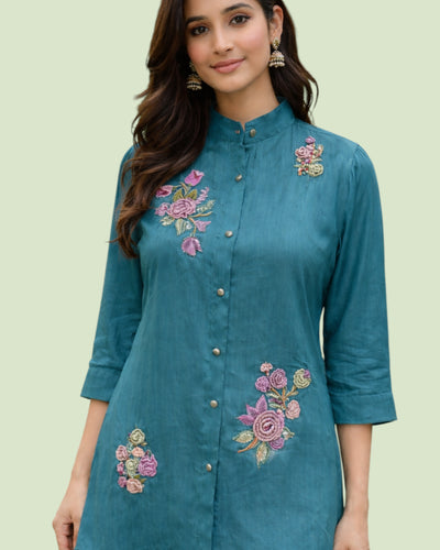 Woman wearing a teal kurta with floral embroidery on a light green background