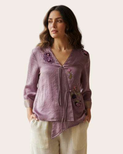 Woman wearing a purple embroidered top with a plain background
