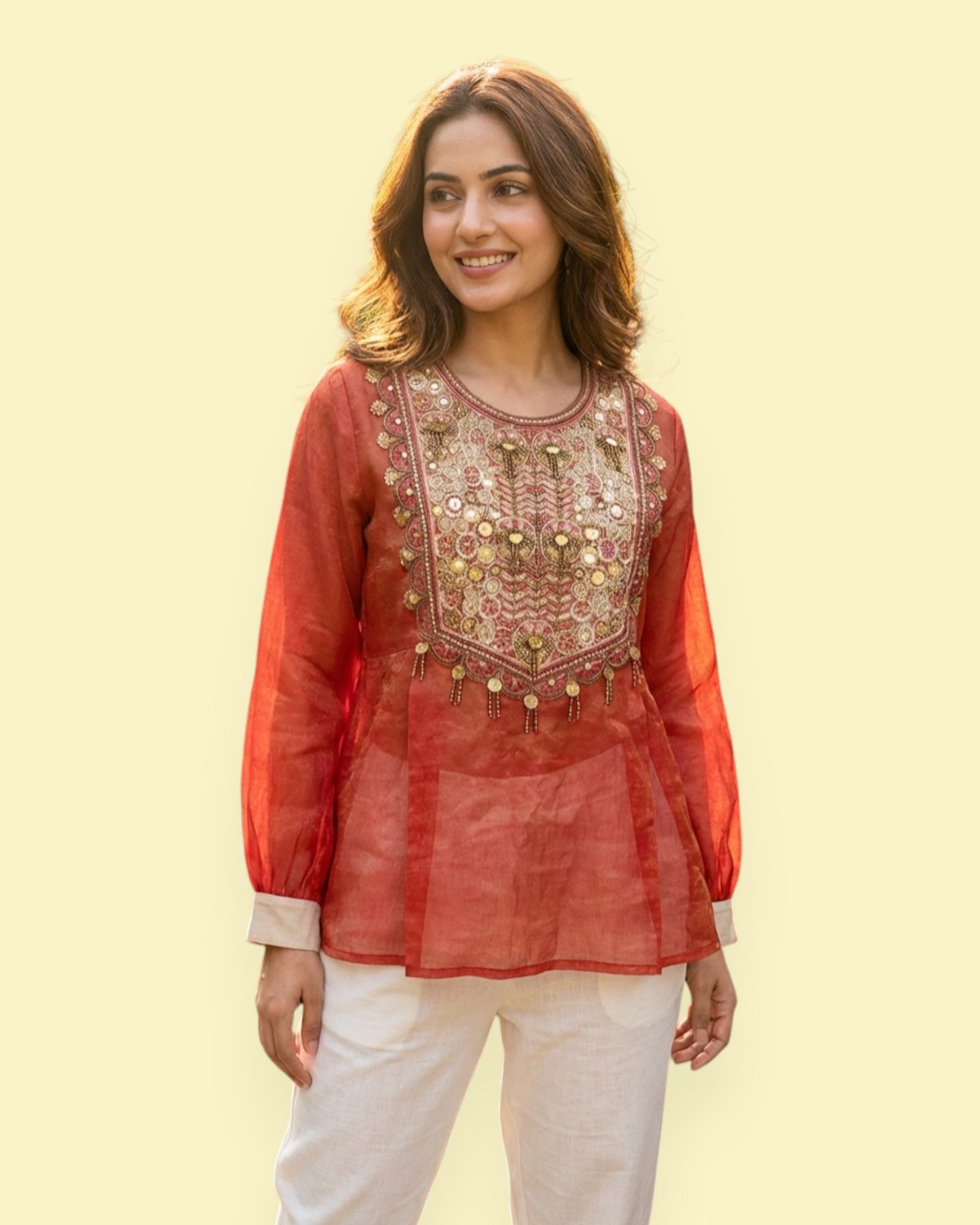 Woman wearing a red embroidered top with white pants on a light yellow background