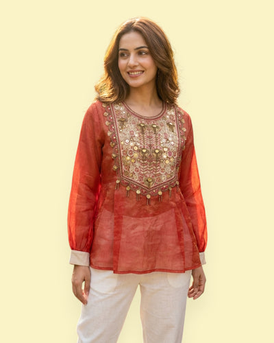 Woman wearing a red embroidered top with white pants on a light yellow background