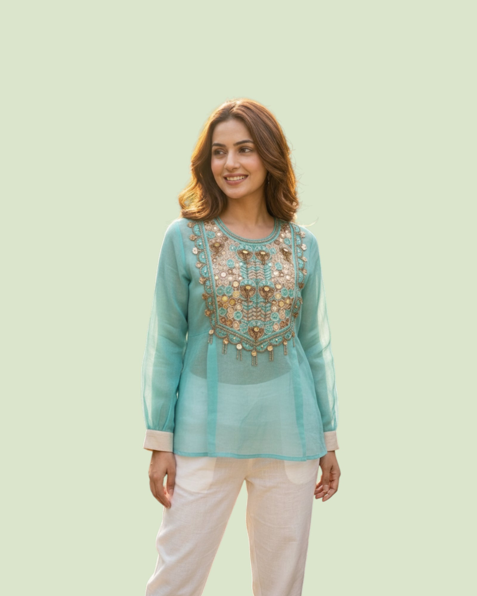 Woman wearing a light blue embroidered top with white pants on a light green background