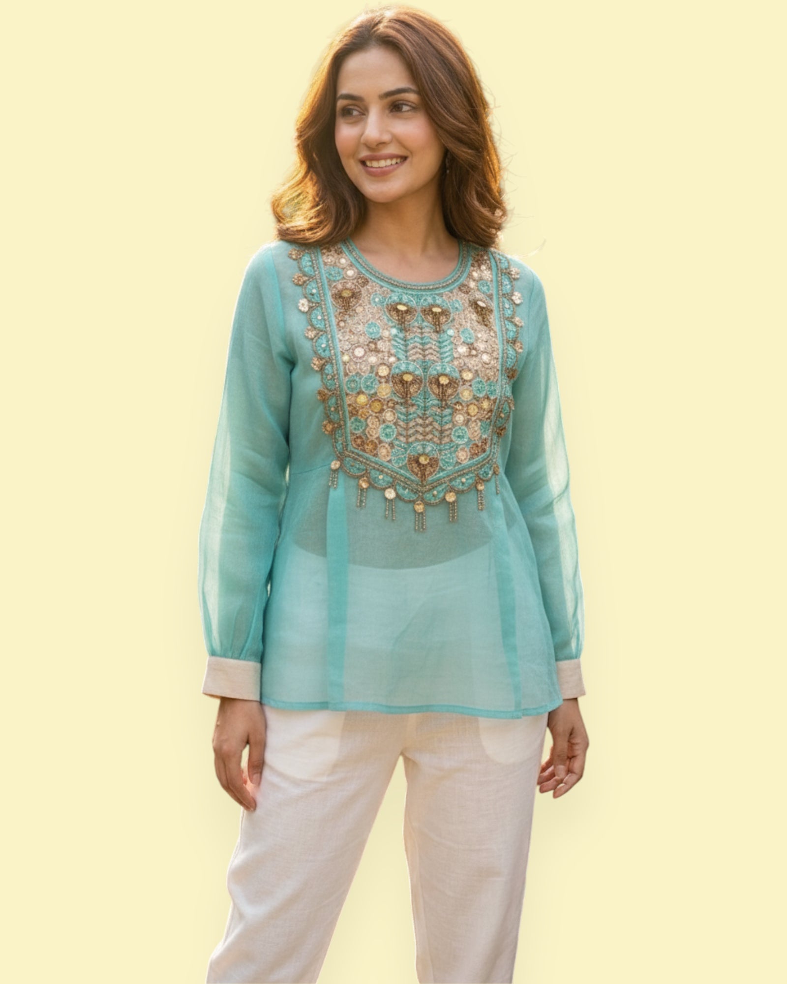 Woman wearing a light blue embroidered top with white pants on a yellow background