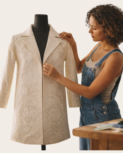 Woman adjusting a beige embroidered coat on a mannequin