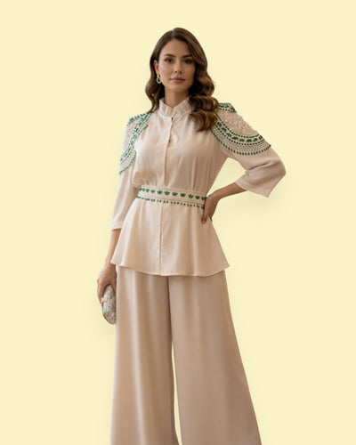 Woman wearing a beige blouse with green embroidery and wide-leg pants on a light yellow background