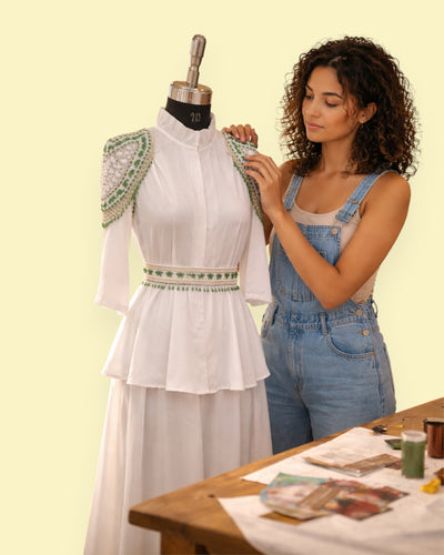 Woman adjusting a white dress on a mannequin with a yellow background