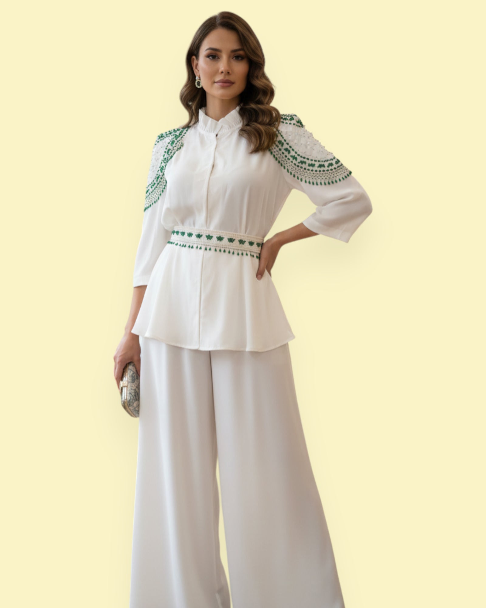 Woman wearing a white blouse with green beadwork and white pants on a light yellow background
