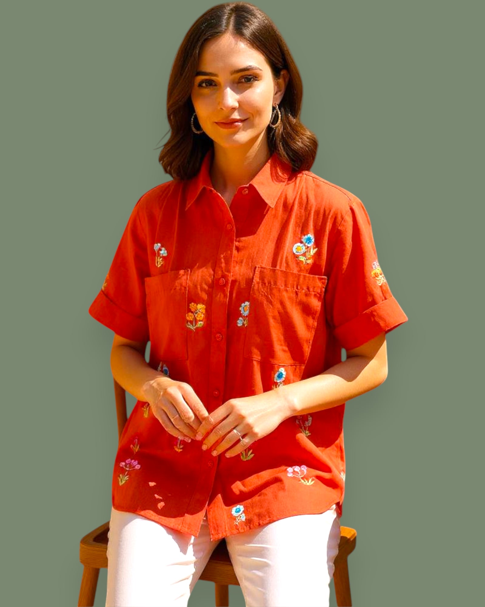Woman wearing a red embroidered shirt sitting on a chair with a plain background
