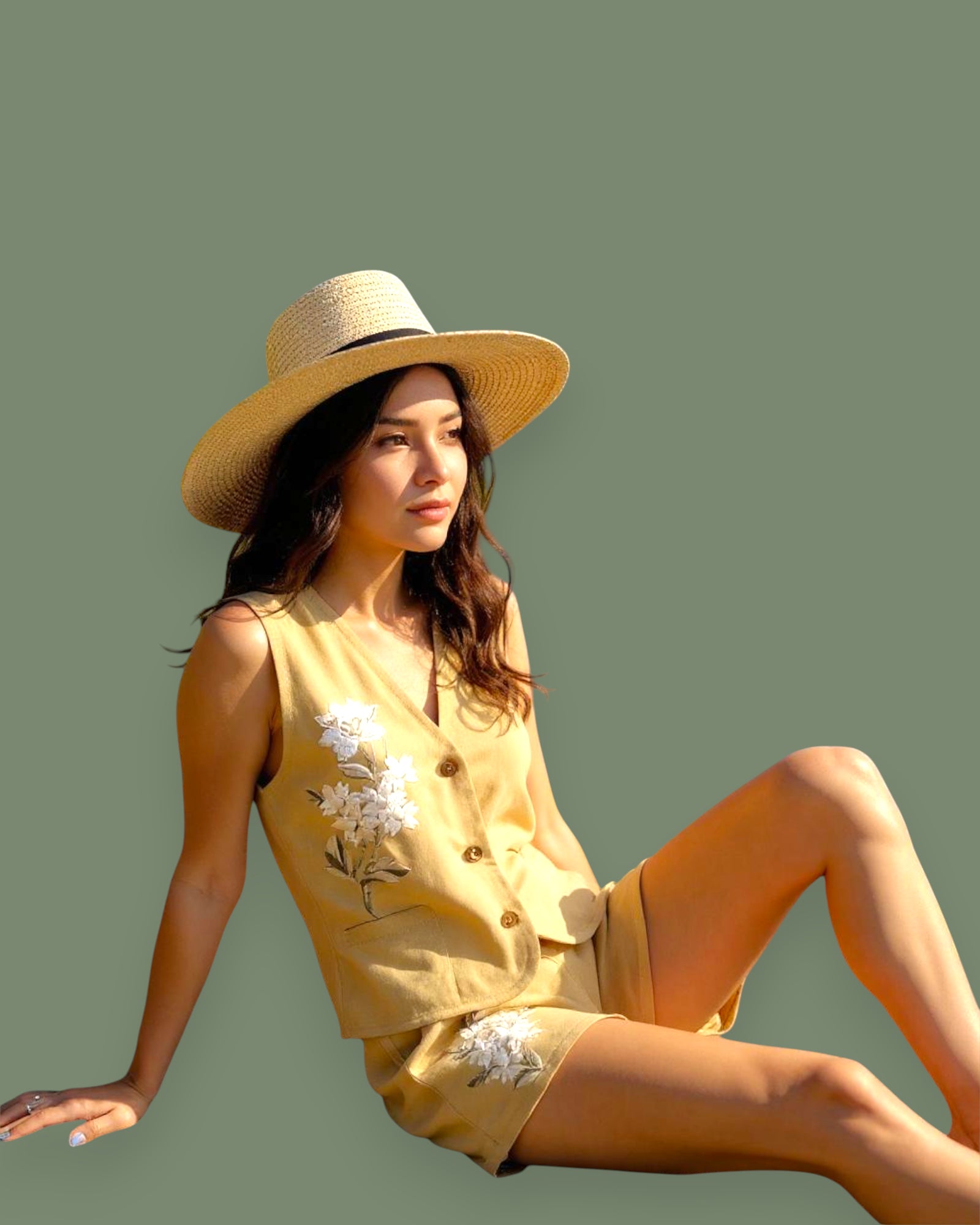Woman wearing a yellow outfit with floral details and a straw hat on a green background
