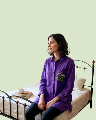 Woman in a purple shirt Embroidery pocket and sitting on a bed with a light green wall.