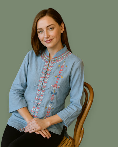 Woman wearing a blue embroidered shirt sitting on a wooden chair against a green background