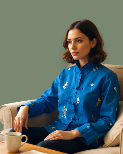 Woman wearing a blue embroidered shirt sitting on a couch with a green background