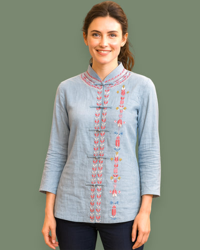 Woman wearing a light blue embroidered shirt on a dark green background