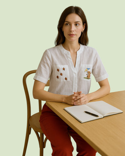  wearing a white linen shirt with embroidery and red linen pant. Woman sitting at a table with a notebook and pen,