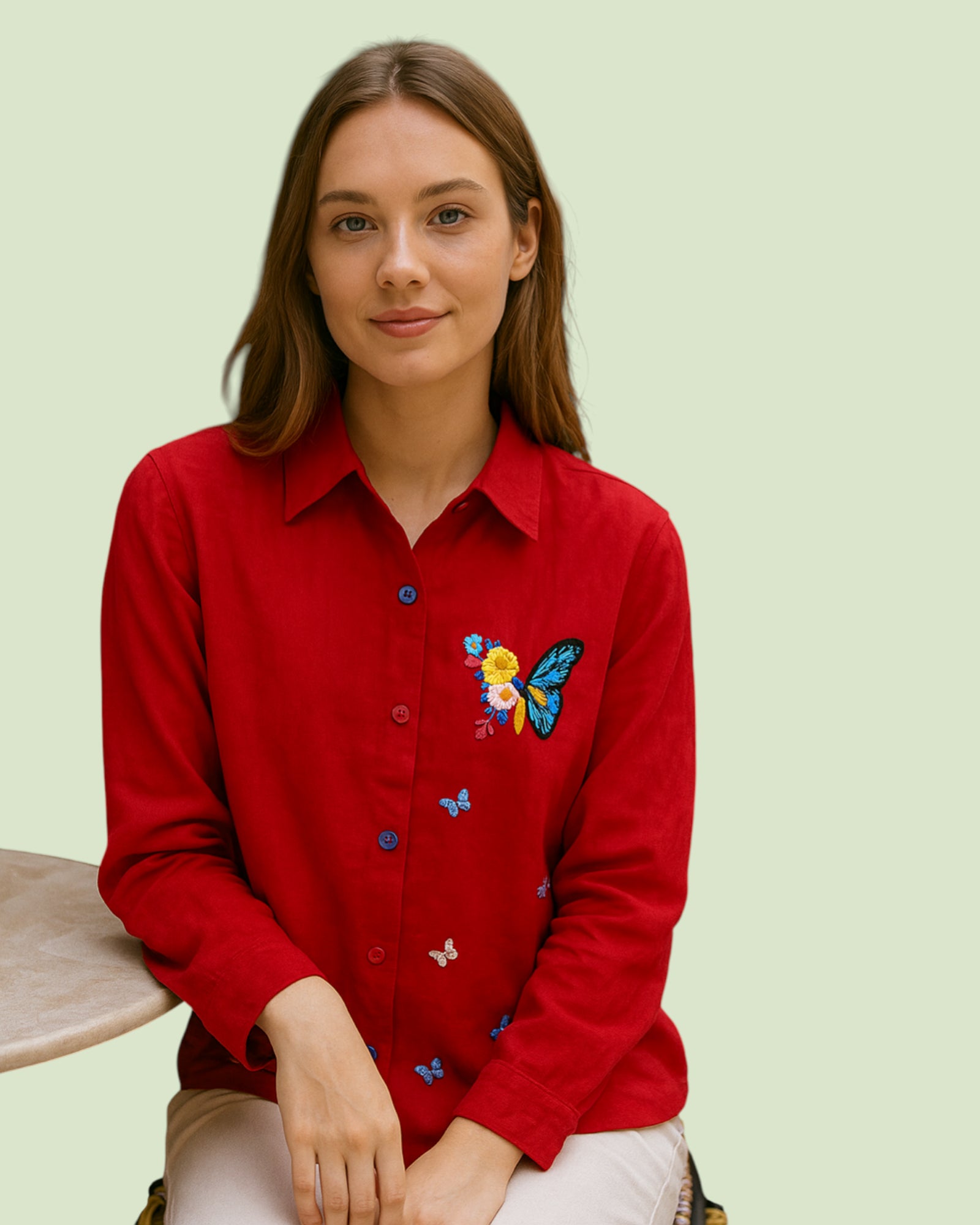Woman wearing a red shirt with floral and butterfly embroidery on a light green background