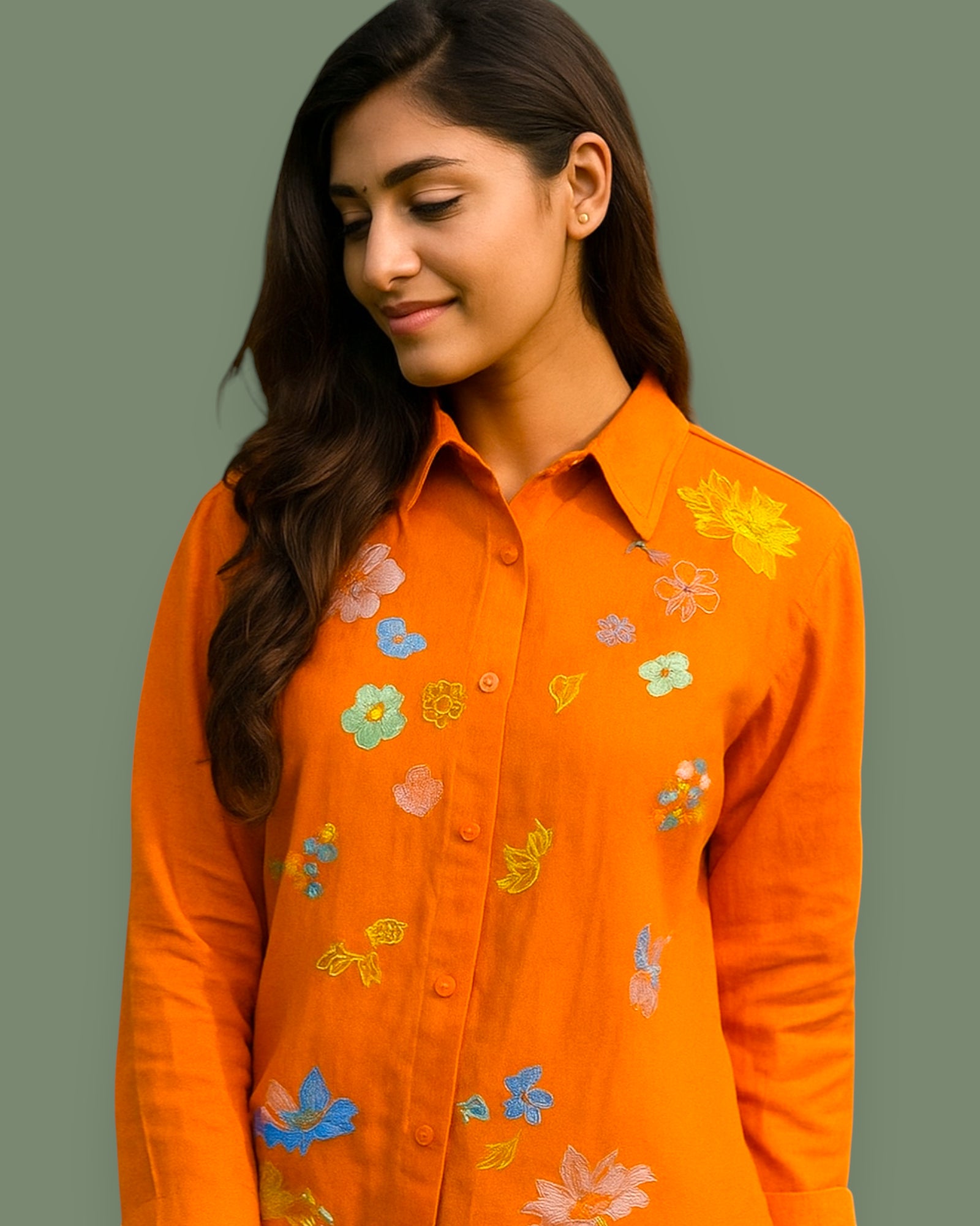 Woman wearing an orange shirt with floral embroidery on a gray background
