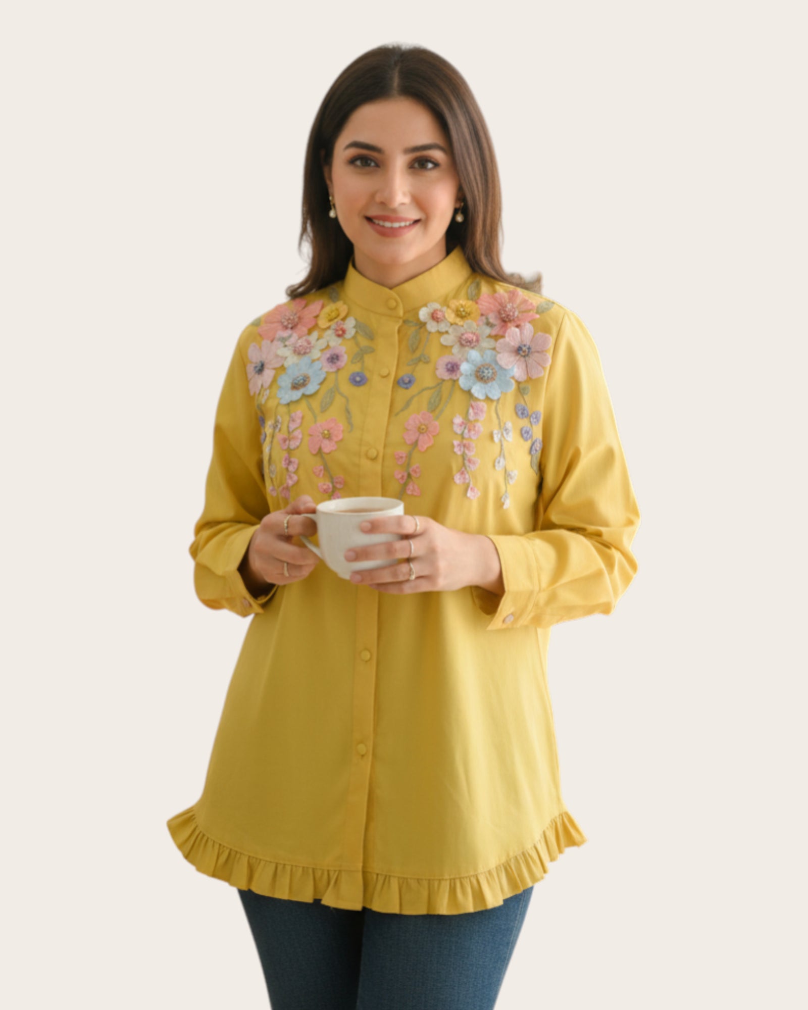 Woman wearing a yellow embroidered Floral shirt holding a cup against a white background