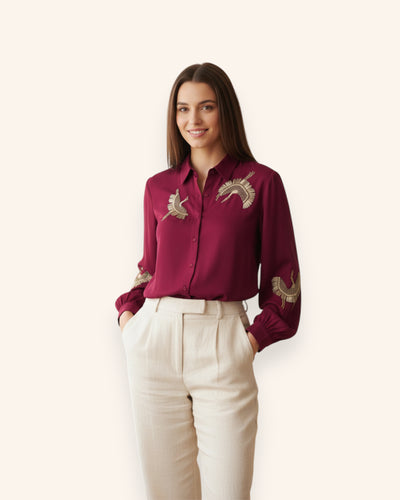 Woman wearing a burgundy embroidered shirt and white pants on a white background