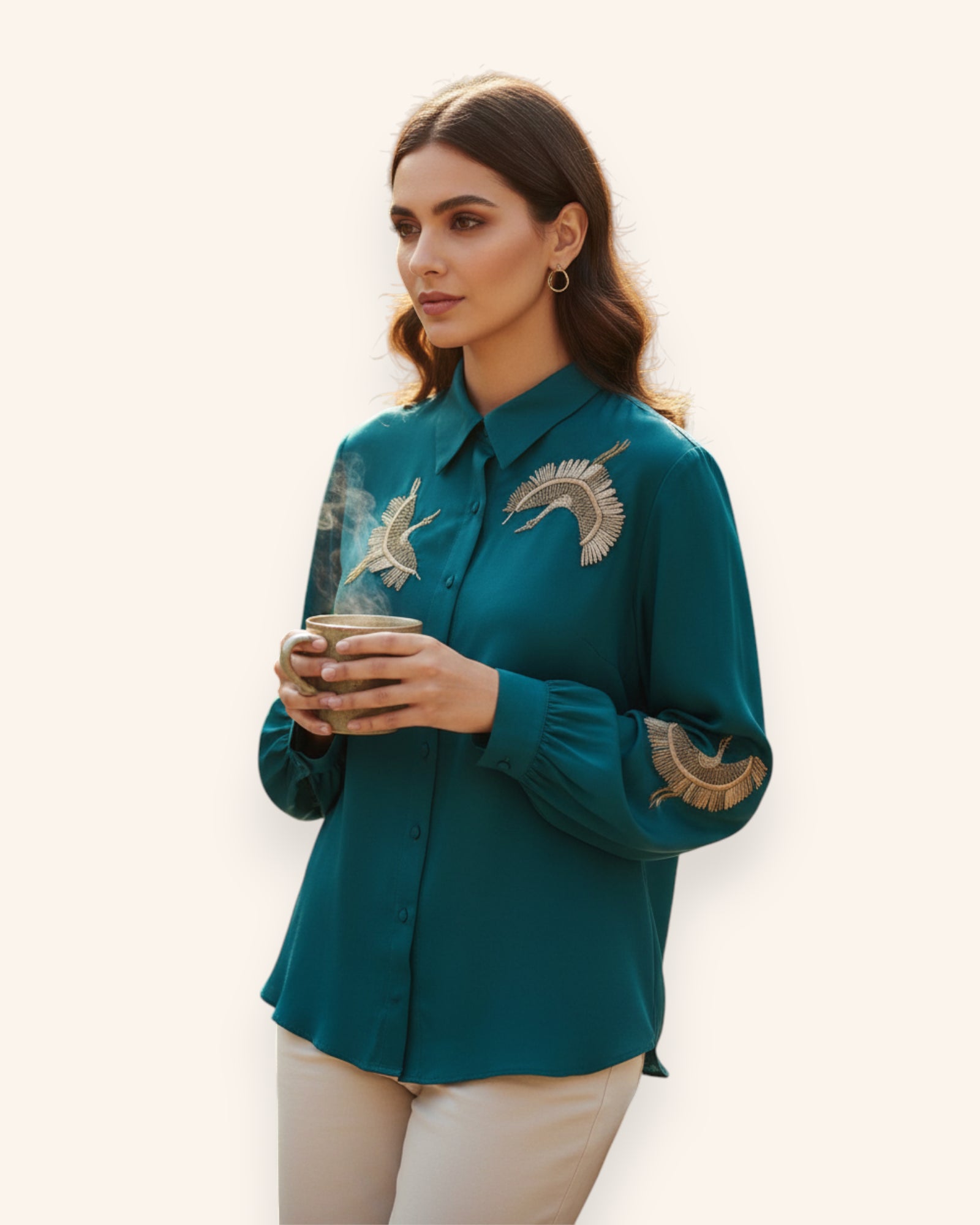 Woman wearing a teal shirt with embroidered designs, holding a cup.