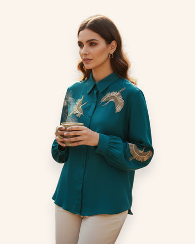Woman wearing a teal shirt with embroidered designs, holding a cup.