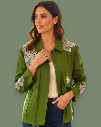 Woman wearing a green jacket with floral embroidery on a solid background