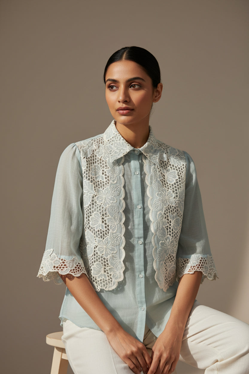 Woman wearing a light blue blouse with lace details against a neutral background