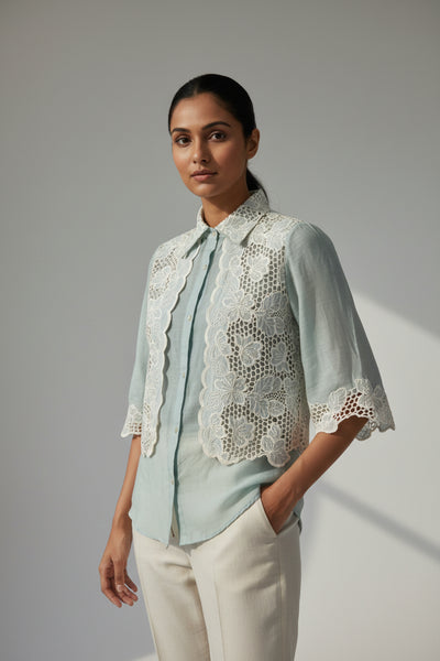 Woman wearing a light blue shirt with a lace-trimmed jacket against a plain background